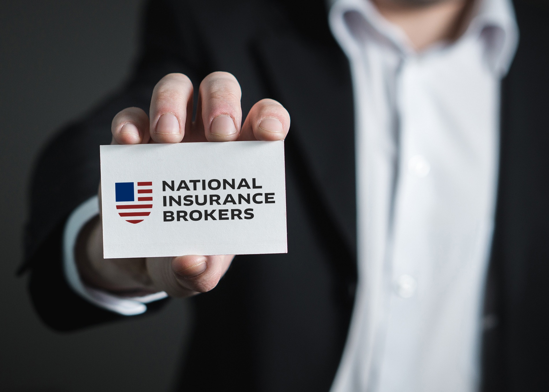 A person in a suit holds a business card featuring a logo with red and blue elements, accompanied by the text "National Insurance Brokers.