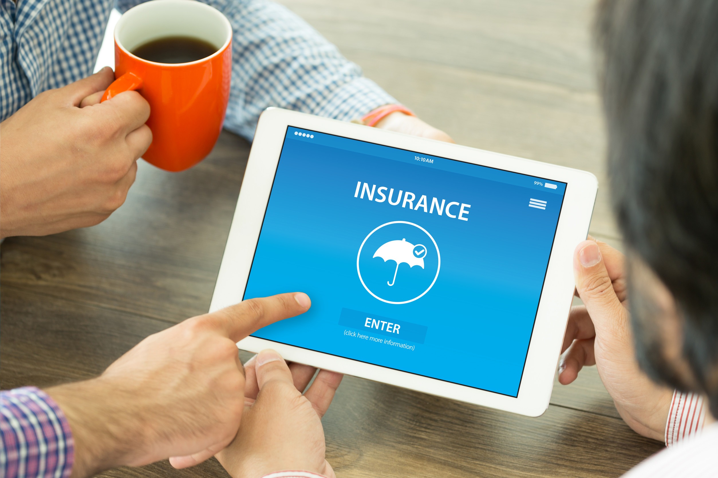 Two people sit at a table; one holds an orange mug while the other taps a tablet displaying a blue screen with the word “Insurance” and an umbrella icon. A finger points at the "Enter" button, hinting at bundling options for home and auto insurance.