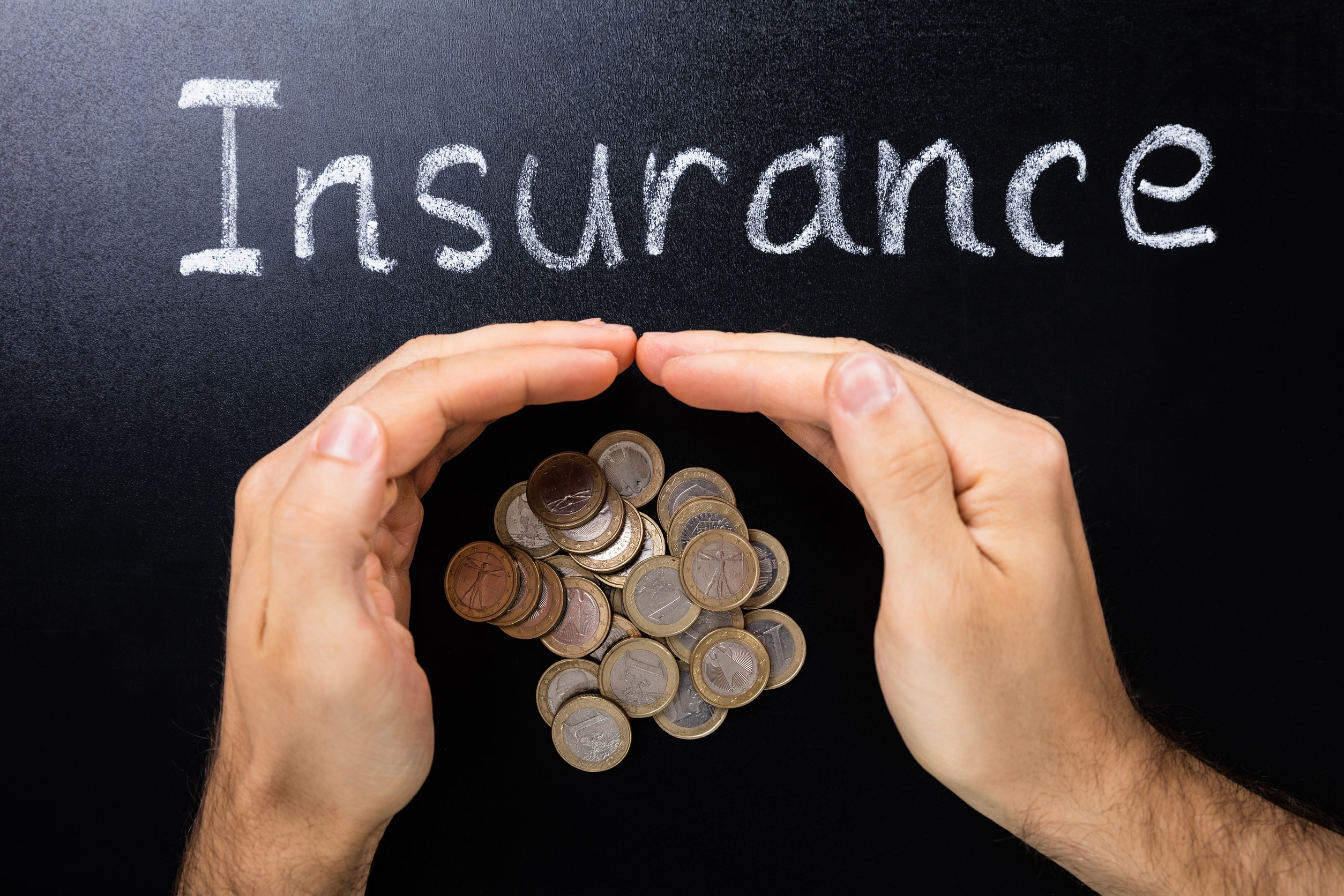 Two hands form a protective gesture over a stack of coins on a black surface, with the word 